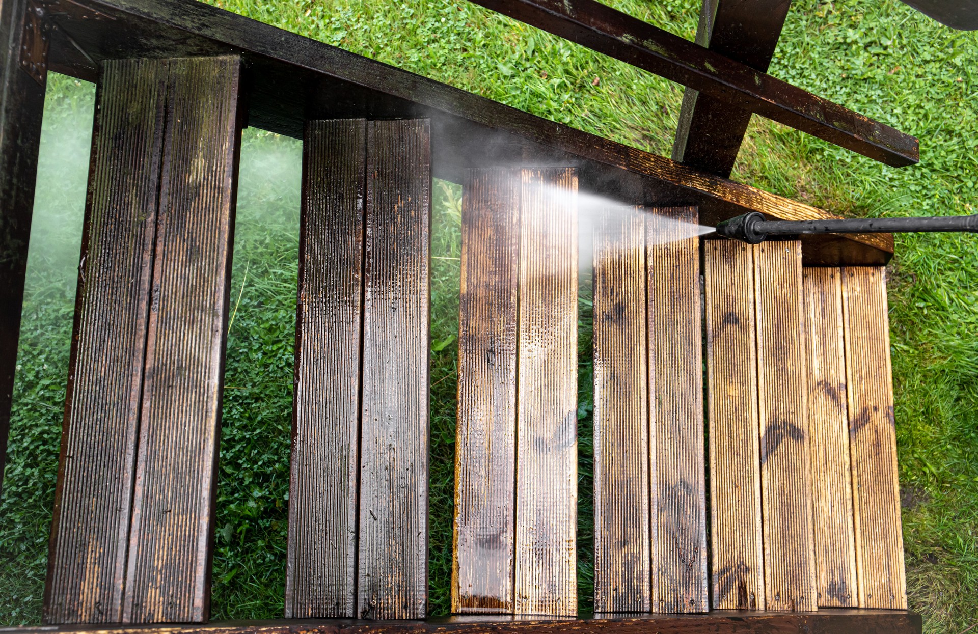 Close up view of using pressure washer to clean impregnated wood terrace stairs outdoors in the spring. Before cleaning and after, big contrast in color.